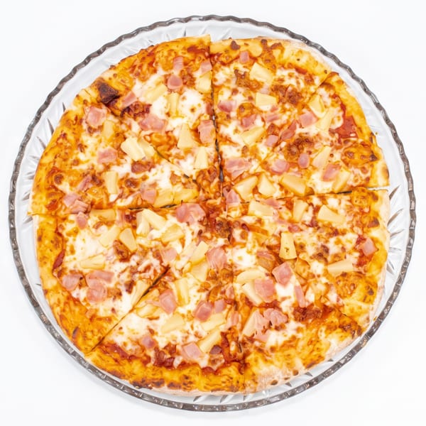 Overhead view of a whole Hawaiian pizza with ham and pineapple on a clear glass plate.