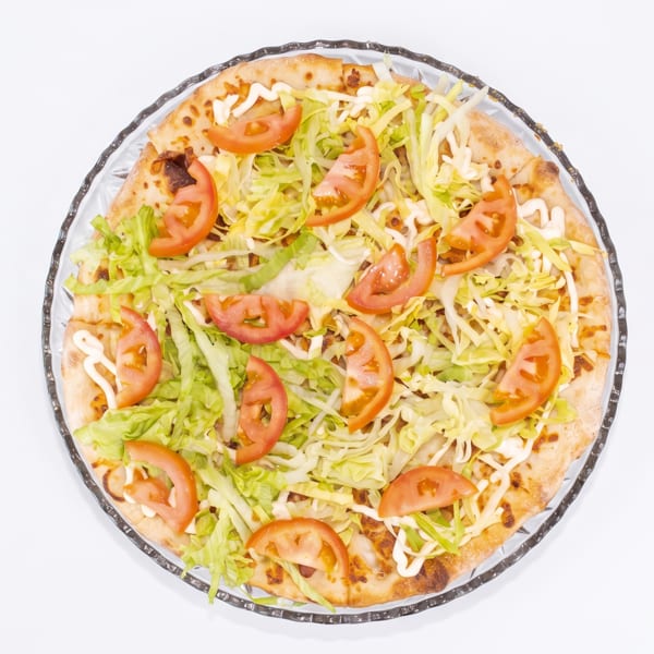 Overhead view of a pizza topped with shredded lettuce, tomato slices, and a drizzle of white sauce.