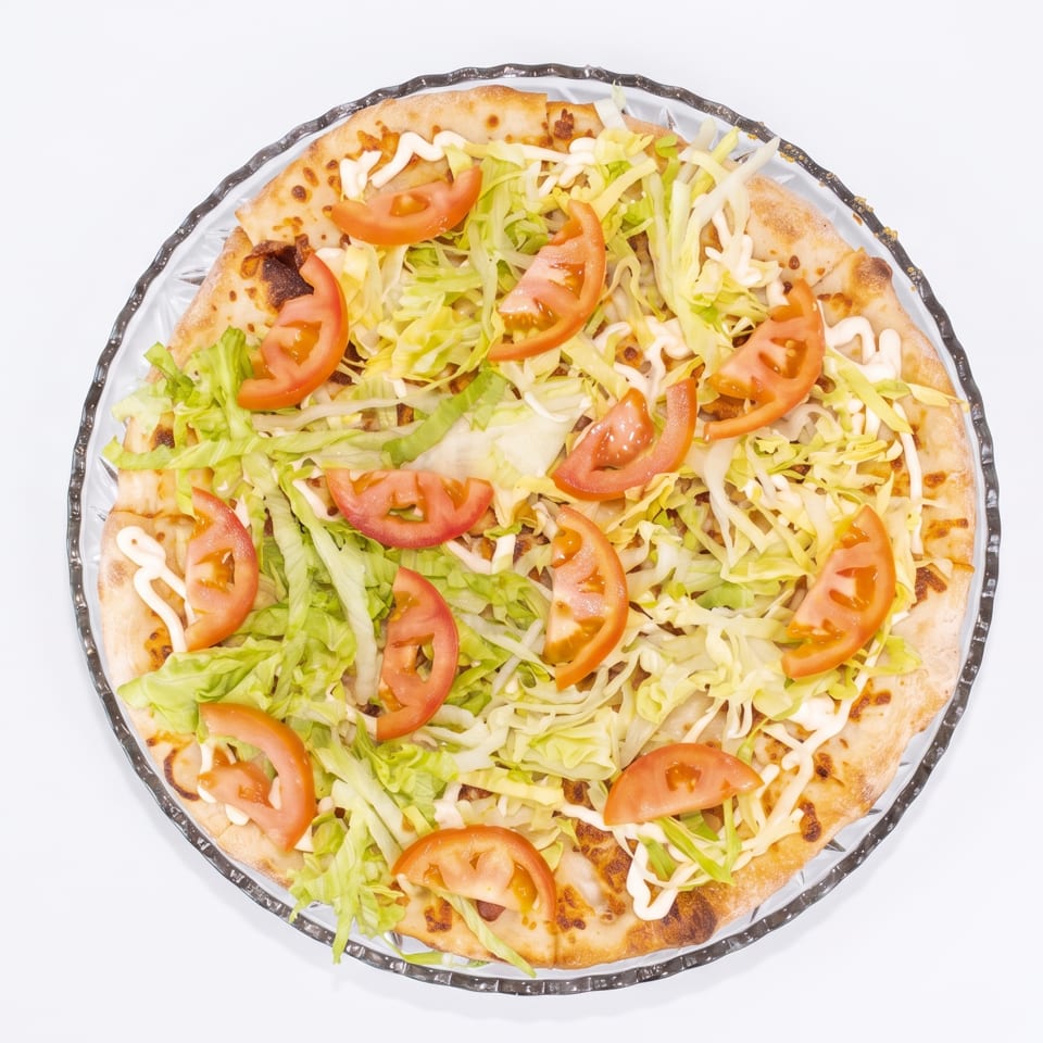 Overhead view of a pizza topped with shredded lettuce, tomato slices, and a drizzle of white sauce.