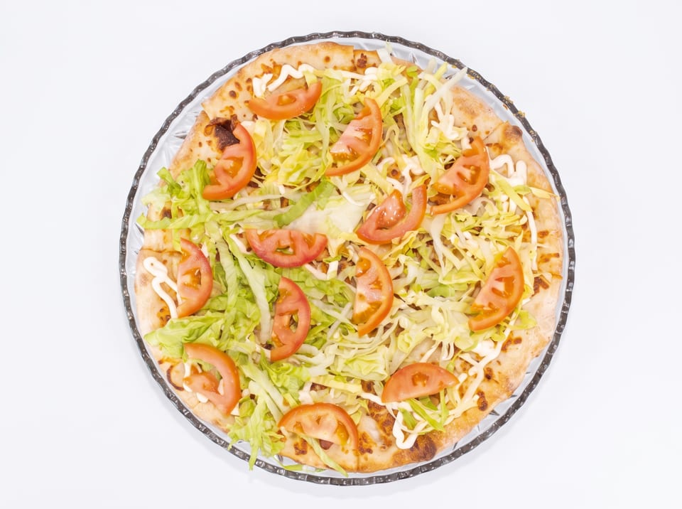 Overhead view of a pizza topped with shredded lettuce, tomato slices, and a drizzle of white sauce.
