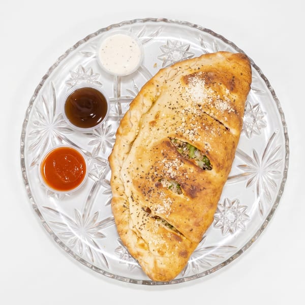 Golden-brown calzone with three dipping sauces on a clear glass plate against a white background.