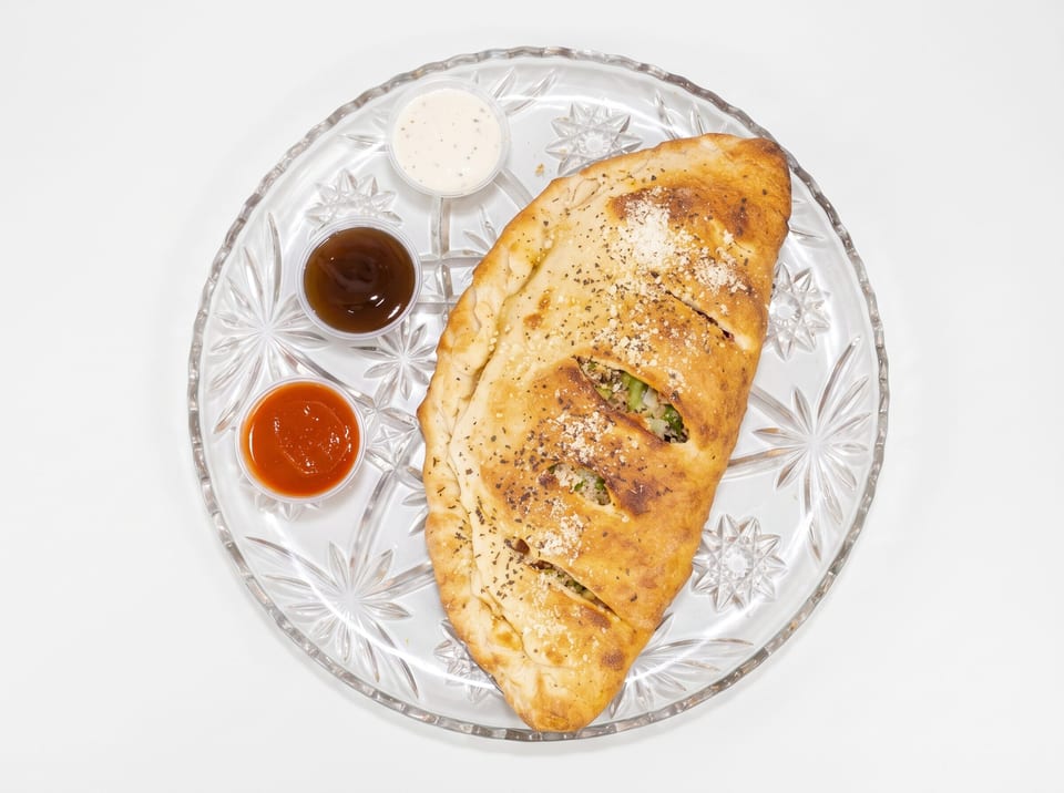 Golden-brown calzone with three dipping sauces on a clear glass plate against a white background.