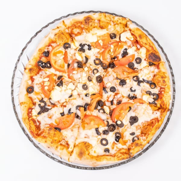 A whole pizza with tomato slices, black olives, and cheese on a clear glass plate.