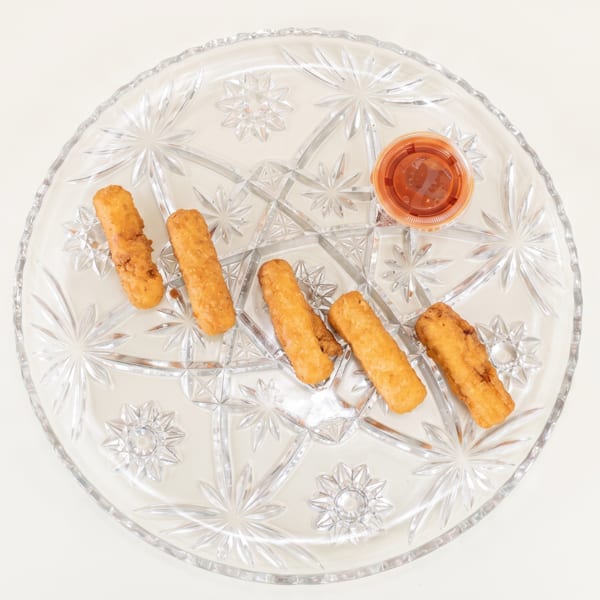 Five golden-brown mozzarella sticks and a small cup of marinara sauce on a clear glass plate.