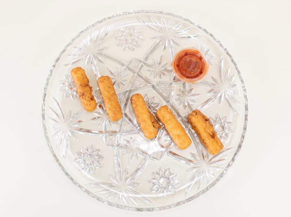 Five golden-brown mozzarella sticks and a small cup of marinara sauce on a clear glass plate.
