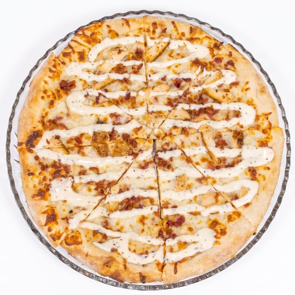 Overhead view of a whole pizza with chicken, bacon, and white sauce, sliced into wedges.