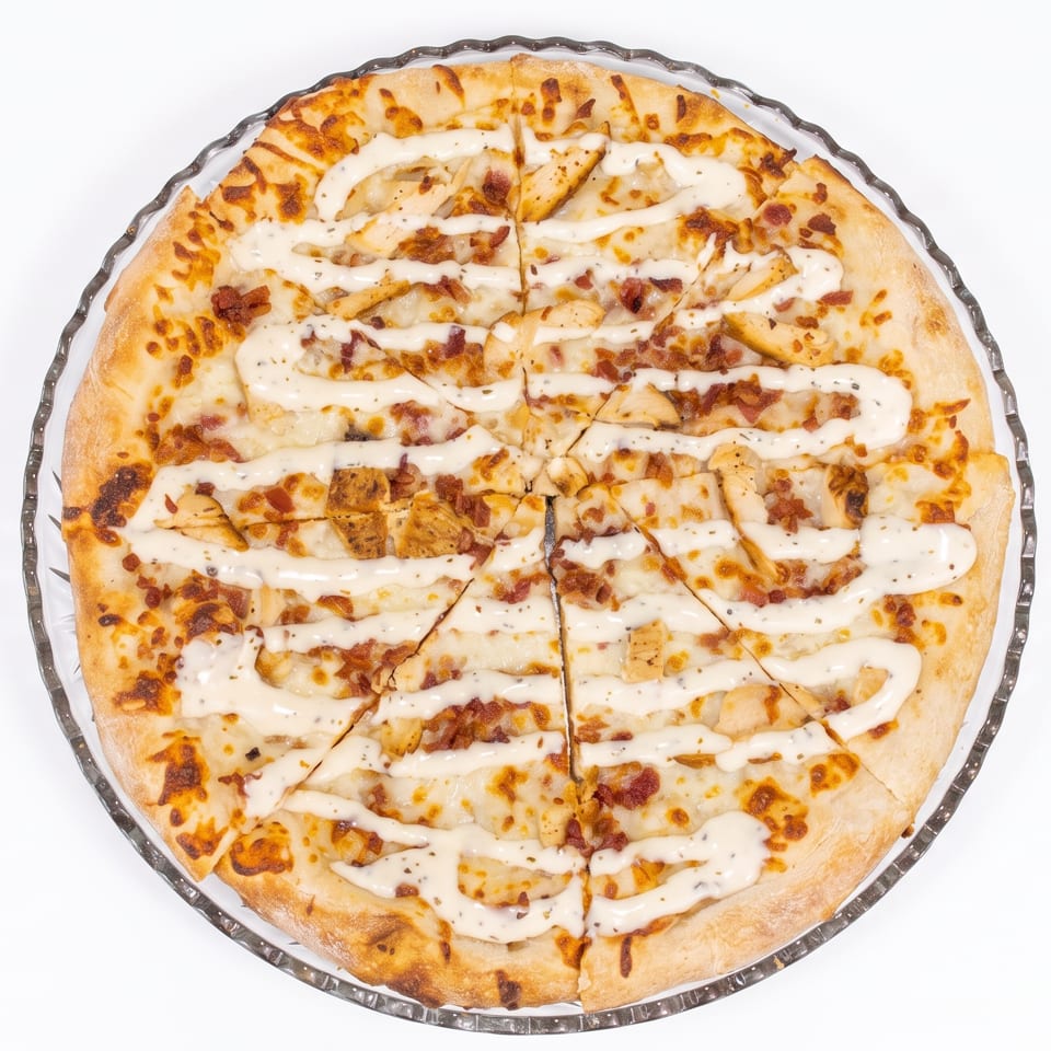 Overhead view of a whole pizza with chicken, bacon, and white sauce, sliced into wedges.