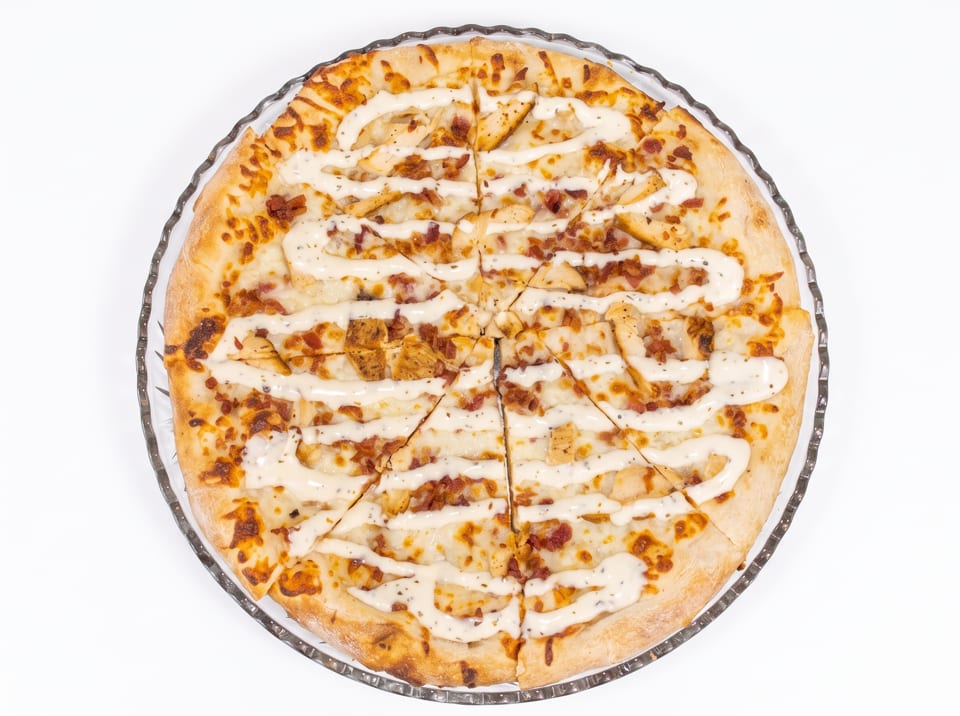 Overhead view of a whole pizza with chicken, bacon, and white sauce, sliced into wedges.