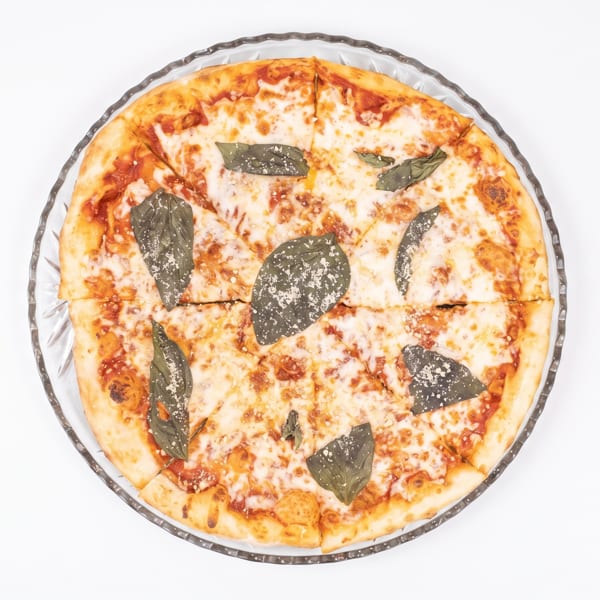 Overhead view of a sliced cheese pizza with basil leaves and parmesan on a glass plate.