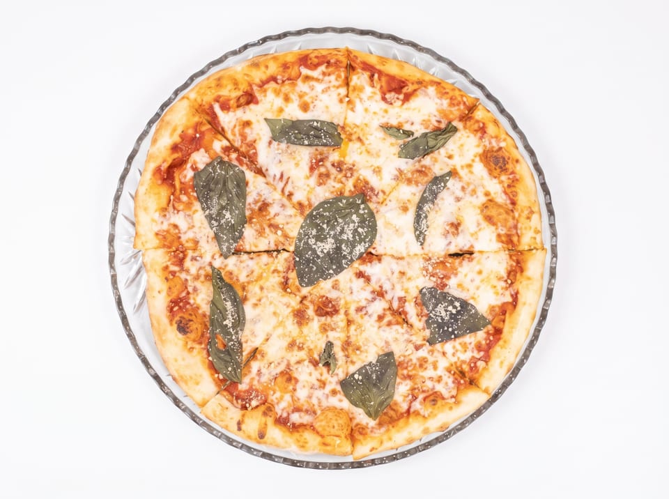 Overhead view of a sliced cheese pizza with basil leaves and parmesan on a glass plate.