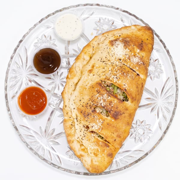 A golden-brown calzone with three dipping sauces on a clear glass plate.