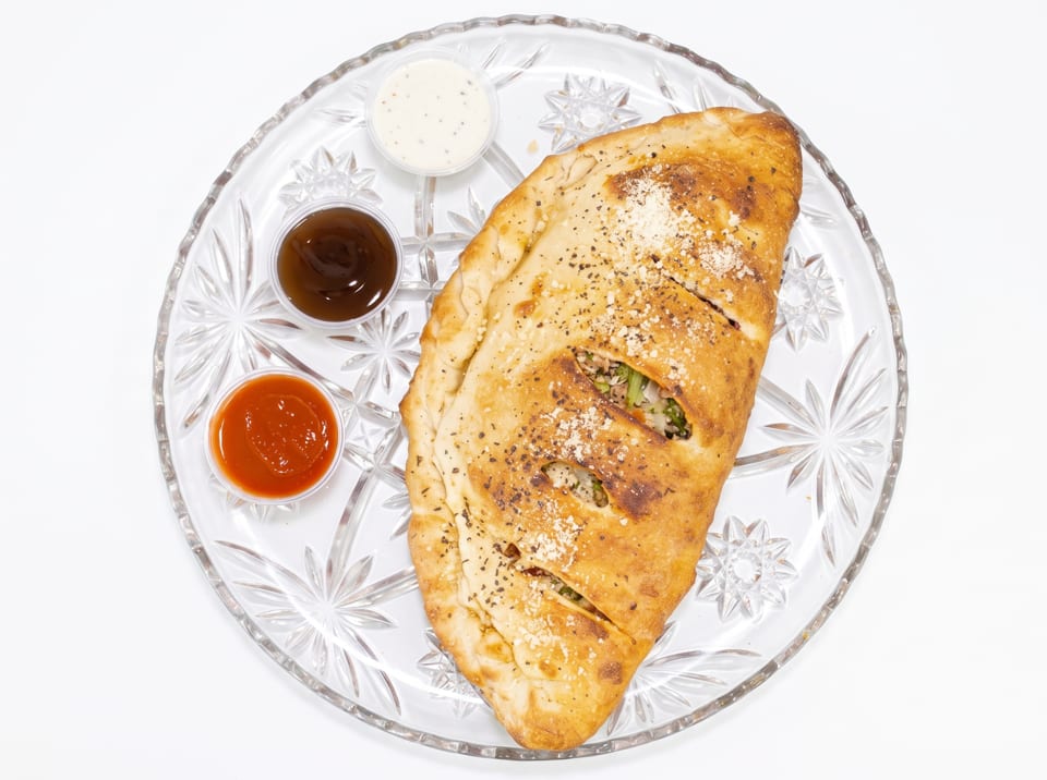 A golden-brown calzone with three dipping sauces on a clear glass plate.