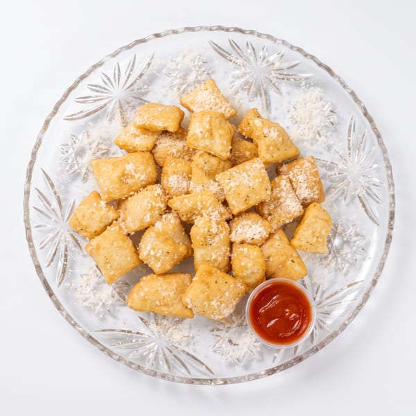 Golden fried pasta chips with parmesan cheese and a side of red dipping sauce on a clear plate.