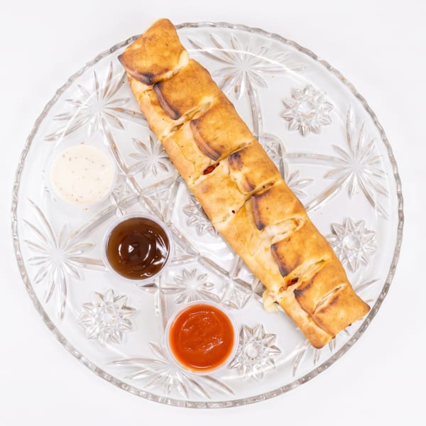 Golden-brown stromboli with three dipping sauces on a clear, patterned glass plate.