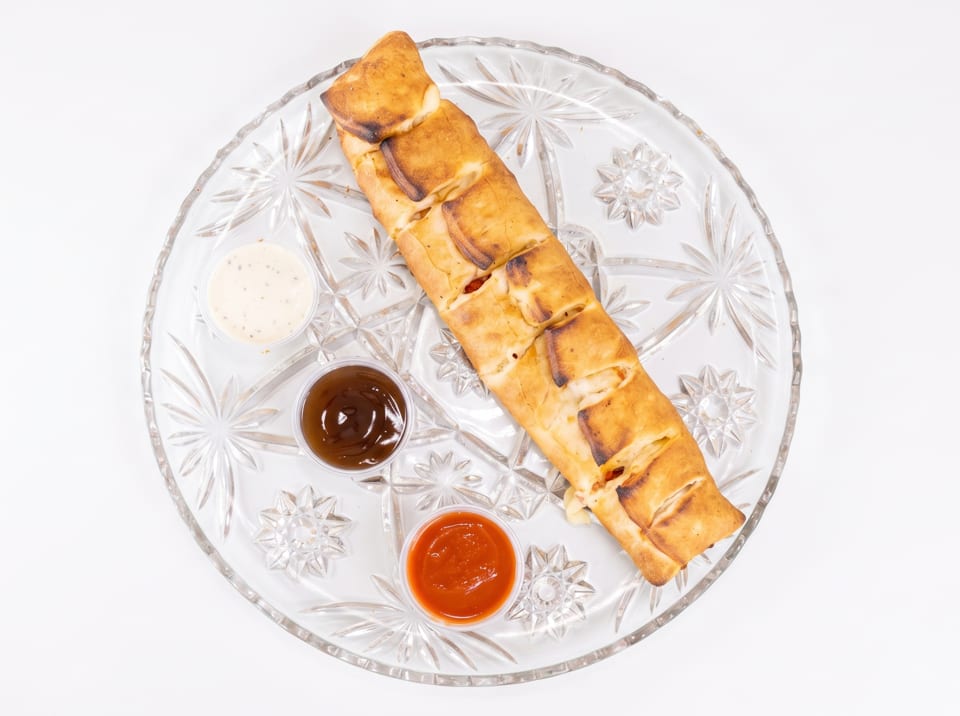 Golden-brown stromboli with three dipping sauces on a clear, patterned glass plate.