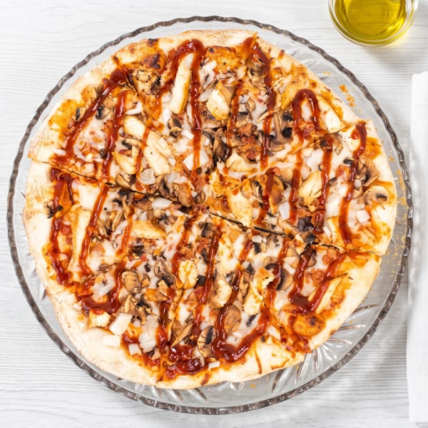 Overhead view of a BBQ chicken pizza with mushrooms and onions on a clear glass plate.