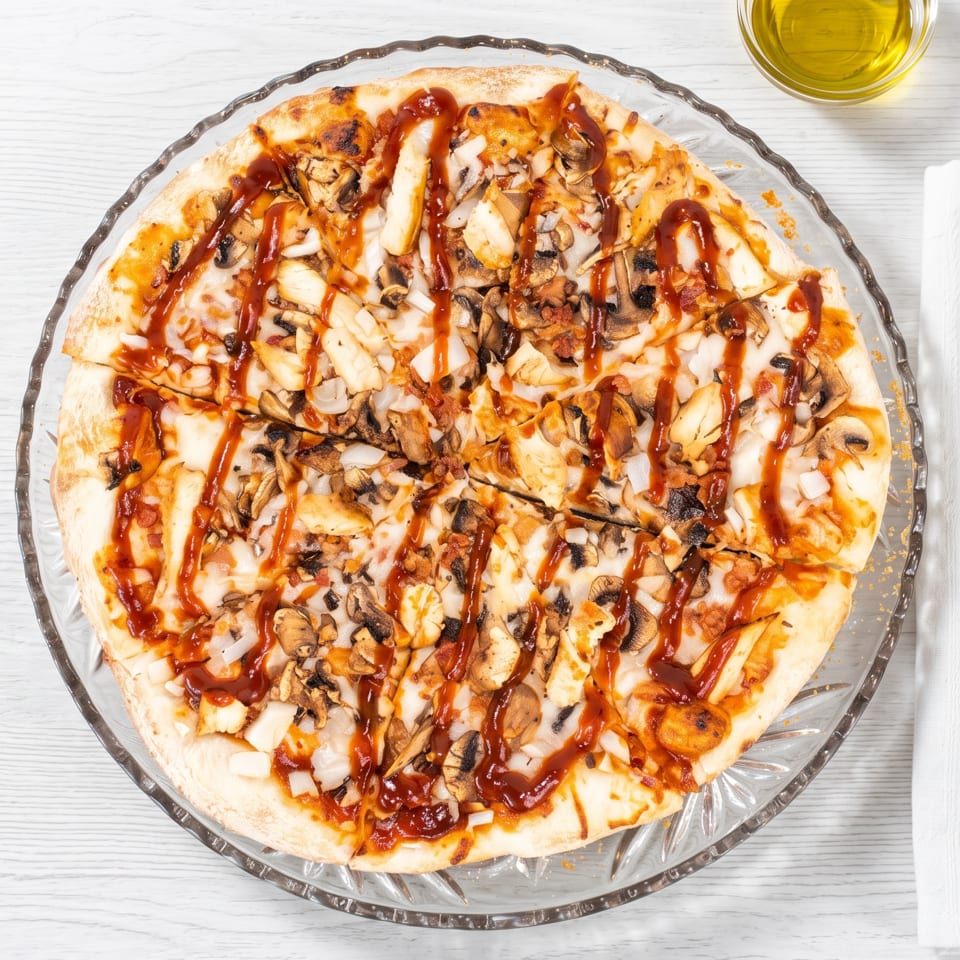 Overhead view of a BBQ chicken pizza with mushrooms and onions on a clear glass plate.