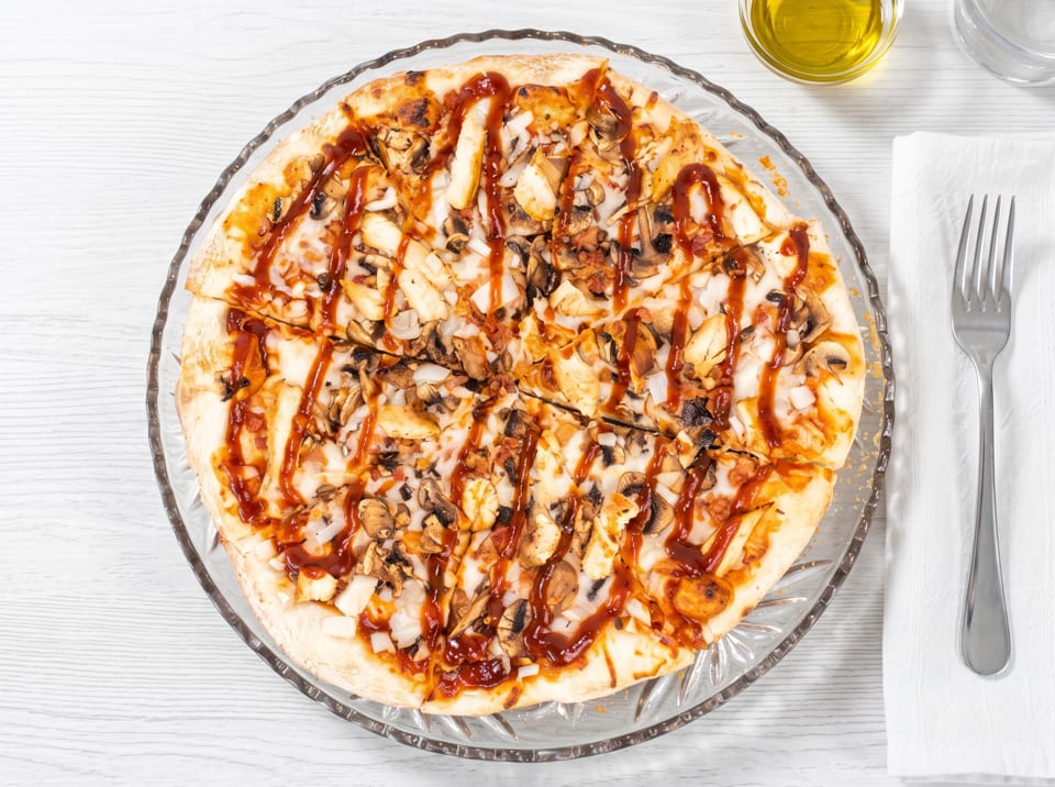Overhead view of a BBQ chicken pizza with mushrooms and onions on a clear glass plate.