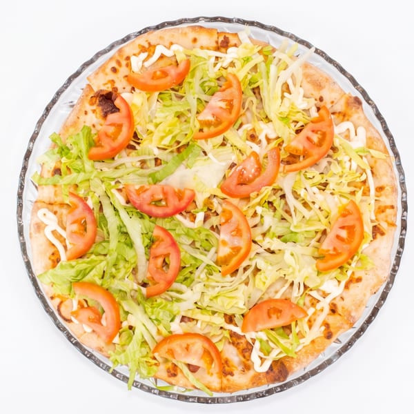 Overhead view of a pizza topped with shredded lettuce, tomato slices, and white sauce on a clear plate.