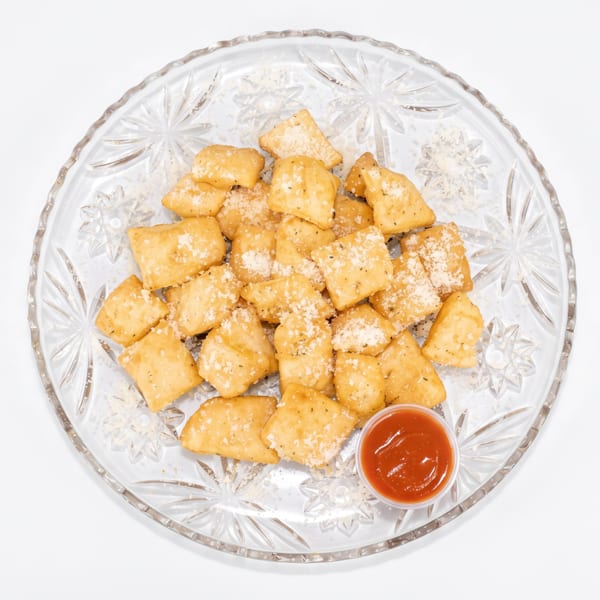 Golden brown fried dough squares, sprinkled with cheese and herbs, served with a side of red sauce.