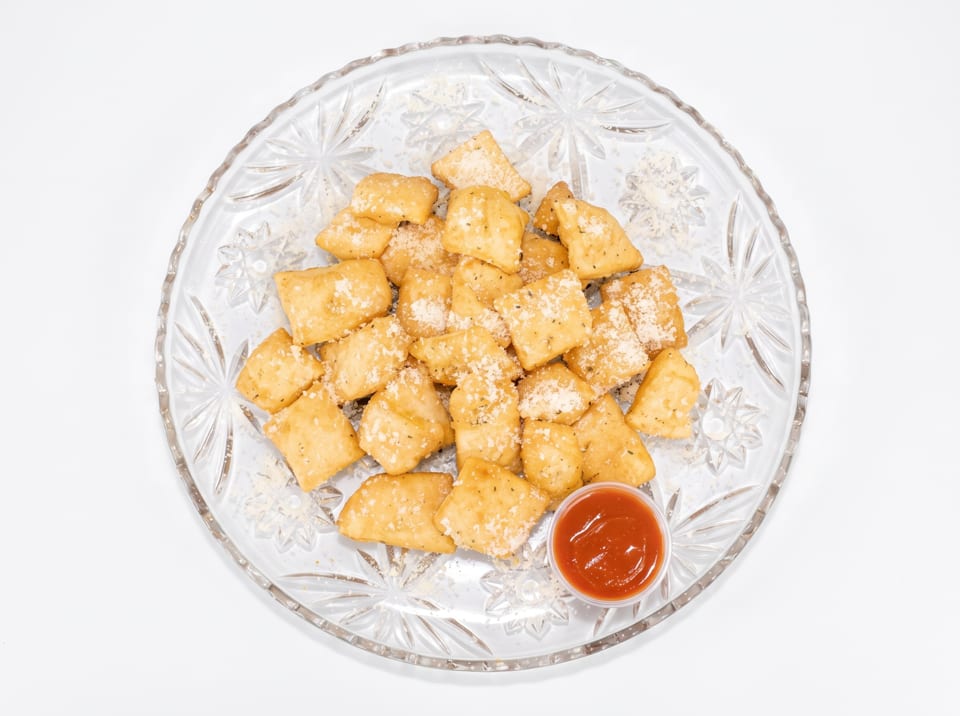 Golden brown fried dough squares, sprinkled with cheese and herbs, served with a side of red sauce.
