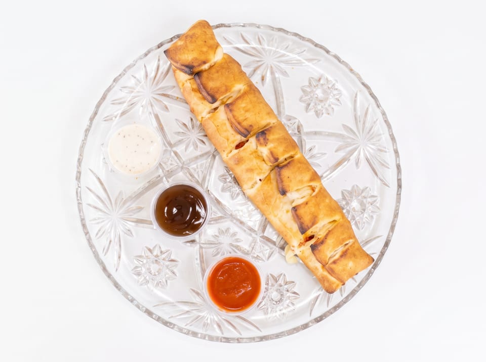 A golden-brown calzone with three dipping sauces on a clear glass plate.